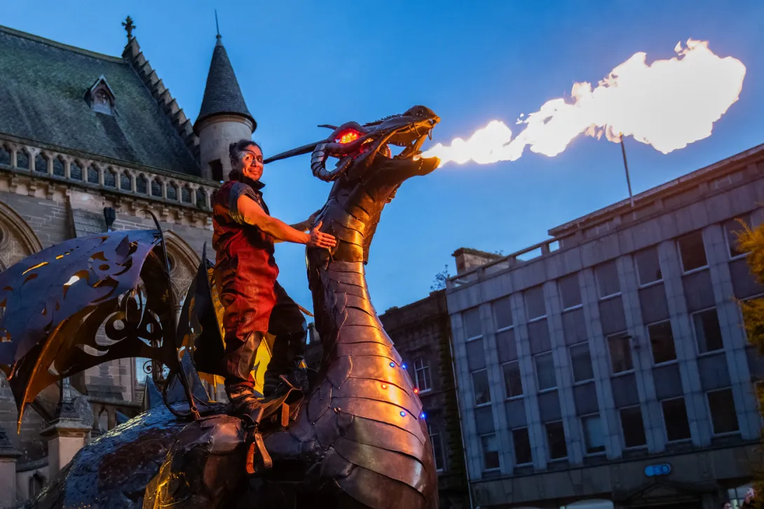Street performer sat on the back of a mechanical, fire-breathing dragon